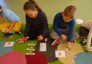Dzieci siedzą na dywanie z rozłożonymi obrazkami, wybierają z pośród różnych herb Warszawy.